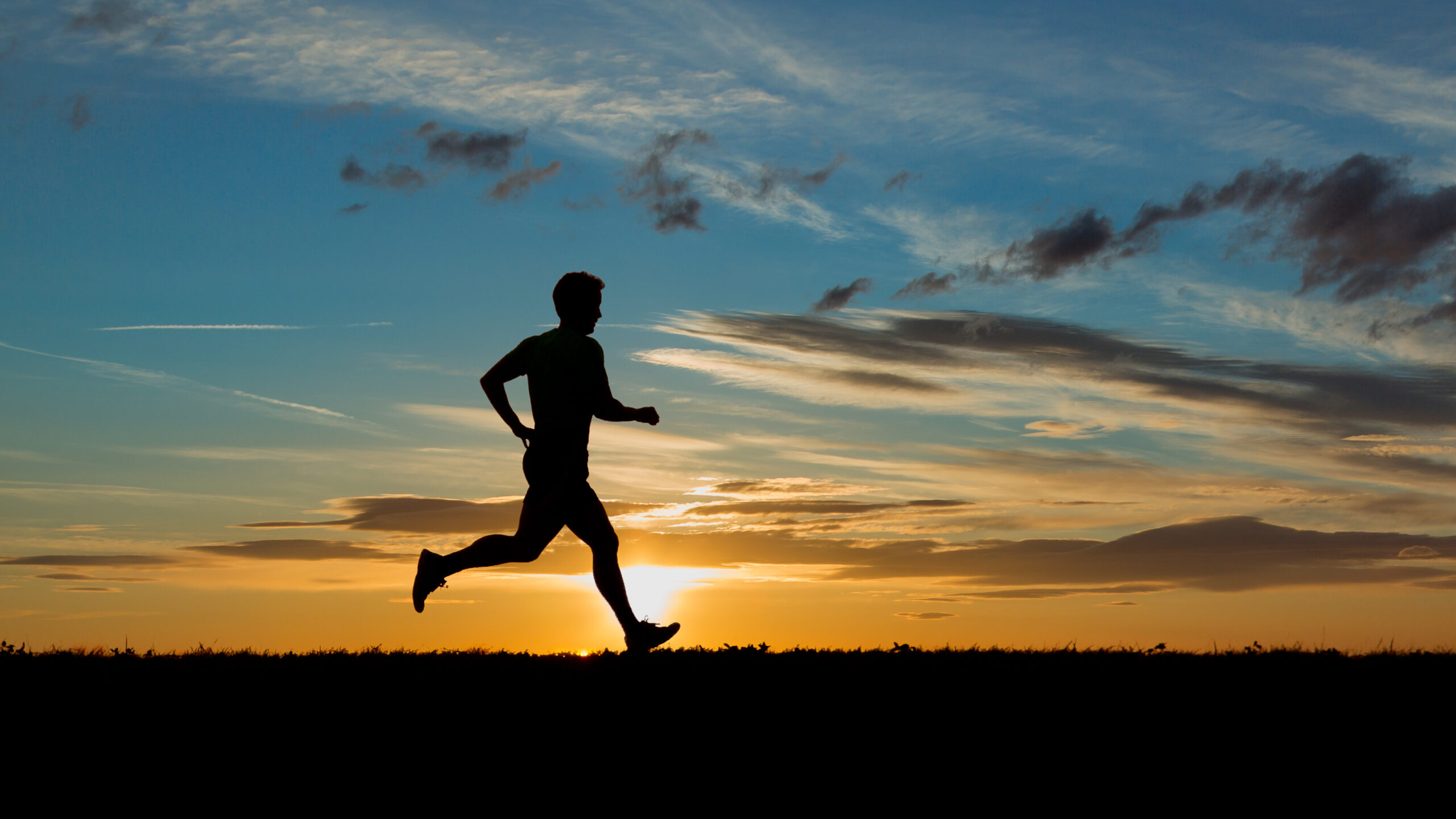 Silhouette of a man running at sunset in an open field.