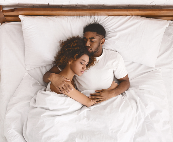 Couple cuddling in bed, eyes closed, relaxed.