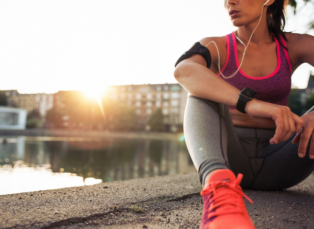 Woman in athletic wear sitting by a lake at sunrise.