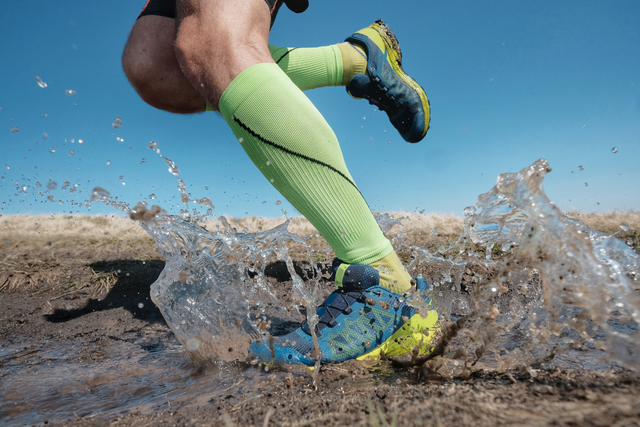 Runner splashing through a muddy puddle in bright socks.