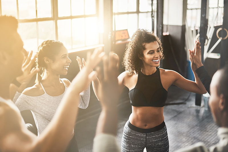 Diverse group of people in athletic gear smiling and giving high fives in a circle, celebrating together after a workout or activity.