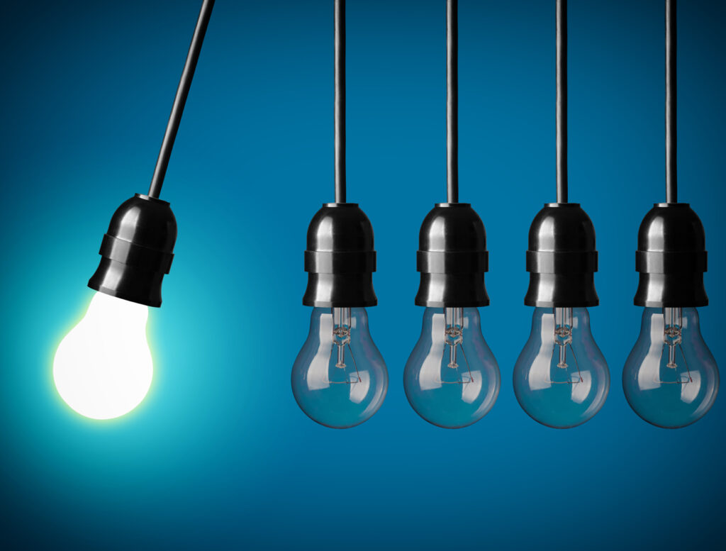 Five light bulbs in a row against a blue background, with the first bulb illuminated and swinging forward while the others remain unlit.