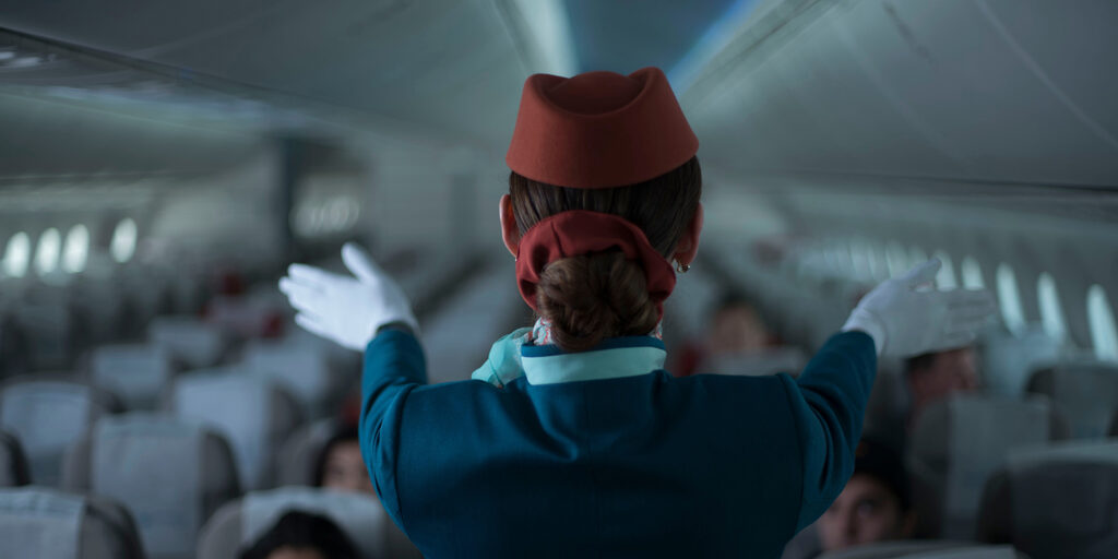 Flight attendant demonstrating safety instructions to passengers inside an airplane cabin