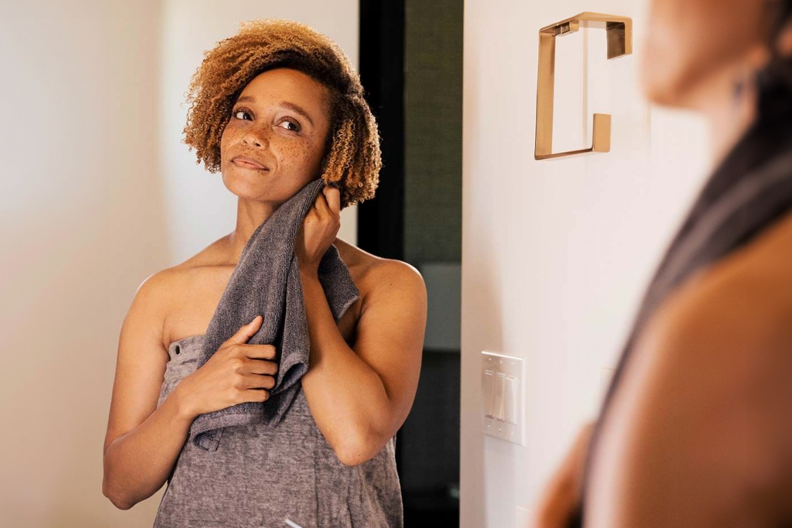 A woman drying her face with a towel in a well-lit bathroom, reflecting self-care and relaxation.