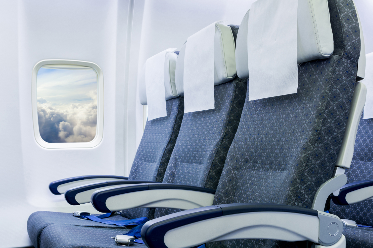 Three empty airplane seats with blue upholstery and white headrest covers next to a window