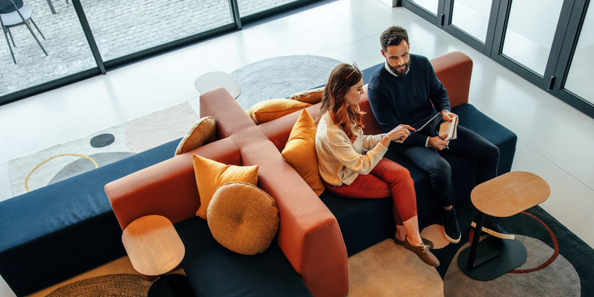 A casual lounge area with a modular sofa in blue and orange, featuring a couple seated and using a tablet.