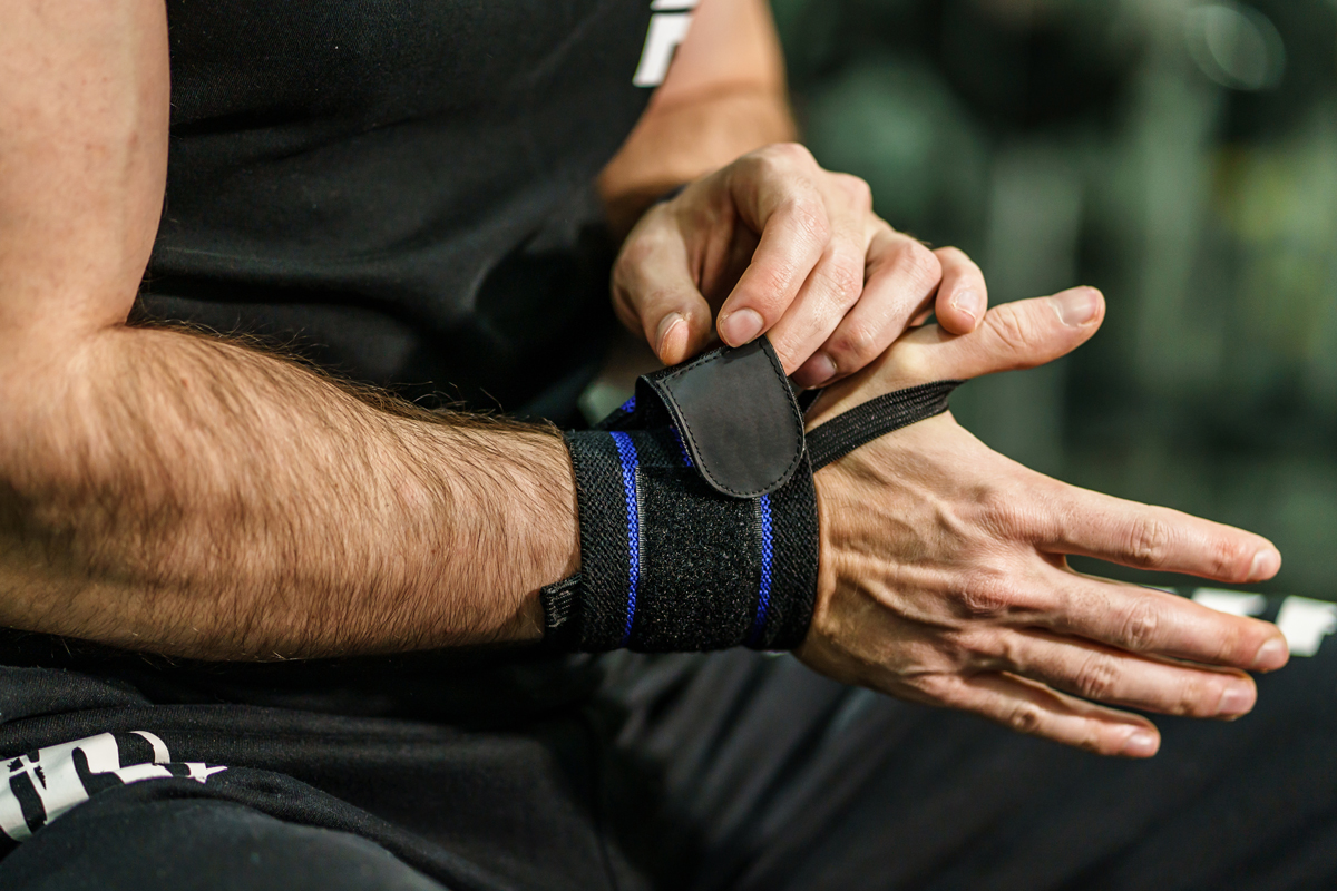 Close-up of a man adjusting a wrist strap while sitting in a gym.