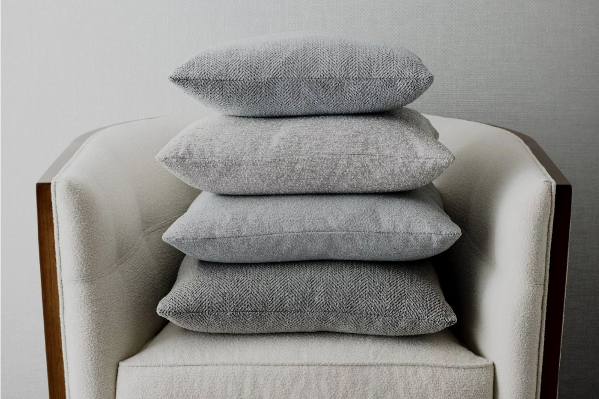 A stack of four gray textured pillows on a white armchair against a neutral background.