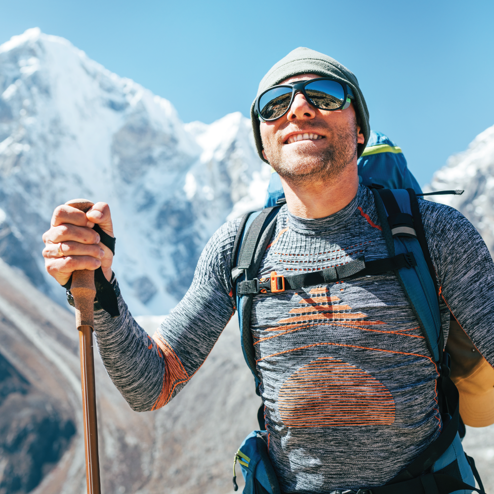 Smiling hiker in sunglasses and winter gear holding trekking poles, standing in front of snowy mountain peaks. Link to visit Celliant's LinkedIn profile.